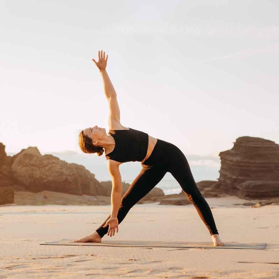 Yogini macht Yoga am Strand und trägt ein schwarzes Outfit von chakrana