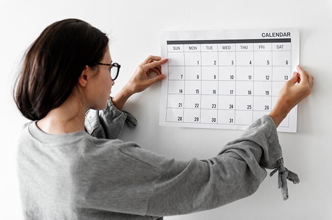 Frau mit Brille hängt Monatskalender an die Wand
