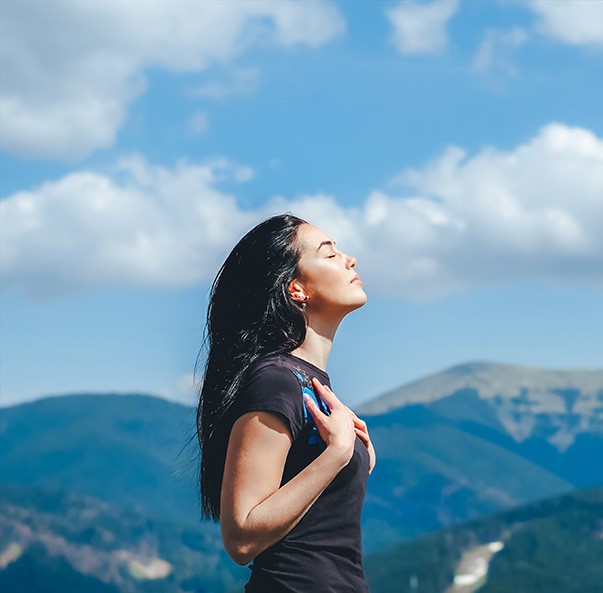 Frau steht unter freiem Himmel auf einem Berg und atmet
