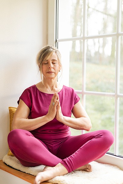 Was ist Achtsamkeit Yogini sitzt auf einer Fensterbank und übt die Achtsamkeitsmeditation in dem chakrana Yoga Overall Saraswati in Beere