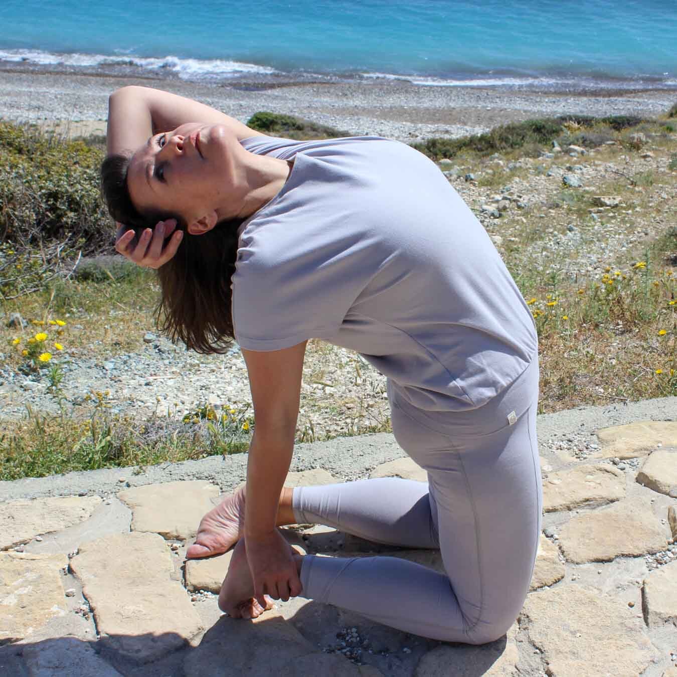 Frau macht draußen am Stradn Yoga und trägt Yogabekleidung aus zertifizierter Biobaumwolle