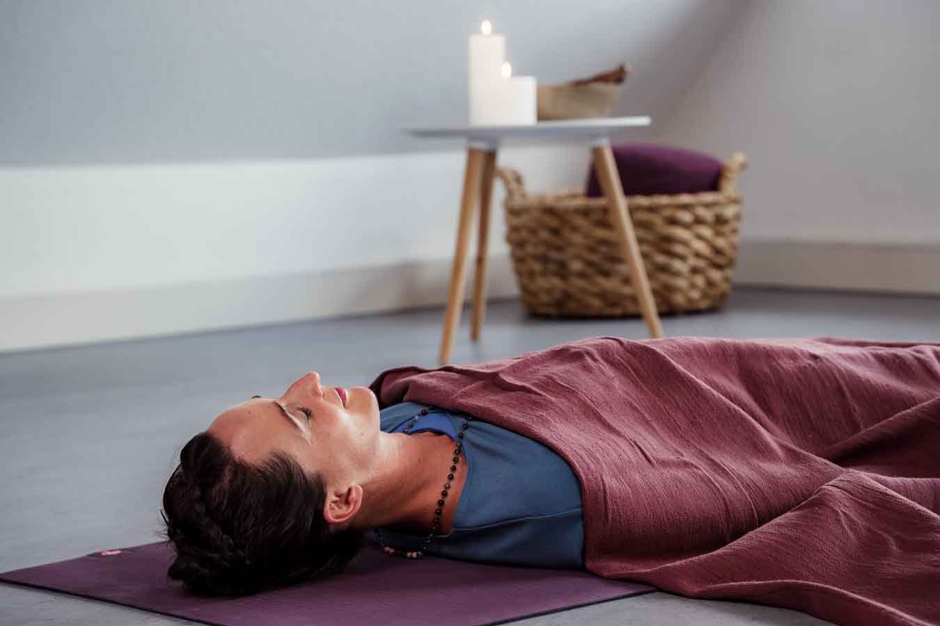 Frau liegt unter einer Decke auf einer Yogamatte in einem Yogastudio und macht Shavasana.